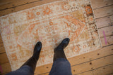 Textured distressed Oushak rug featuring faded ivory and burnt orange geometric patterns.
