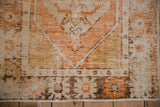 Distressed vintage Oushak rug corner showing wear to foundation, ivory, tangerine, and brown tones.