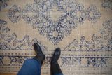 Distressed Oushak carpet showing faded navy medallion, floral motifs, and substantial wear.