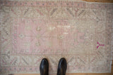 Faded pink and beige distressed Oushak rug, showing even wear, serrated border, and black boots.
