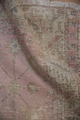 Textural fold of vintage distressed Oushak rug, revealing worn pink and beige pile.