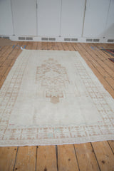 Distressed Oushak rug showing worn ivory pile, geometric border, and faint foundation.