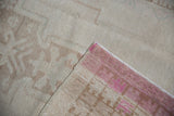 Folded distressed Oushak rug corner showing even pile wear, faint foundation, and pink reverse.
