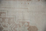 Distressed Oushak runner pile with even wear, faded primitive motifs in soft ivory and pale brown.