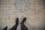 Distressed Oushak rug texture showing worn ivory and blue patterns with exposed foundation.