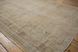 Distressed vintage Oushak carpet with faded ram's horn scroll motifs and low pile.