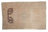 Distressed vintage Oushak rug, faded cream field, subtle aubergine spandrels, and prominent abrash.