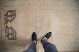 Textured cream field and dusty aubergine corner spandrel of a vintage distressed Oushak rug.