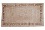 Vintage distressed Oushak carpet with a stepped medallion and floral border in a neutral sand and beige palette.