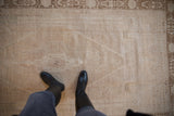 Detail of the distressed Oushak rug's even wear, showing the low pile and pale sand-colored field.