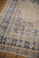 Distressed Oushak rug corner featuring navy serrated floral border and time-softened pile.