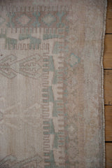 Distressed Oushak rug's original selvage and low pile, featuring muted seafoam hook-and-latch motifs.