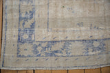Worn corner of a distressed Oushak rug, showing the blue border and exposed knot heads.