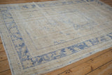 Angled view of a vintage Oushak carpet, highlighting its distressed texture and faded blue border.