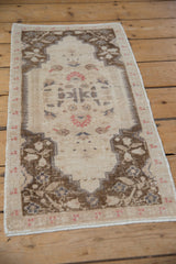 Vintage Oushak rug mat viewed from an angle, showing the floral bouquet and brown spandrels.