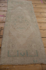 Distressed vintage Oushak mat runner with faded ivory and soft sage floral pinwheel motifs.