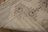 Curled corner of vintage Oushak rug showing antique ivory pile, intact selvage, and woven backing.