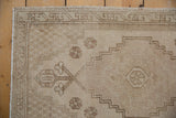 Distressed Oushak rug corner, antique ivory field, faded mauve pinwheel florals, original selvage.