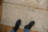 Scale and texture view of a distressed Oushak mat with a low pile in antique ivory and beige.