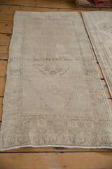 Angled view of a distressed Oushak mat runner showing its faded, abrashed field in soft beige tones.