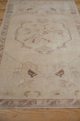 Distressed Oushak rug's textured pile, with faded ivory and mauve floral roundel motif.