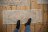 Feet on a distressed Oushak runner, showing faded pink, seafoam blue, and ivory abrashed field.