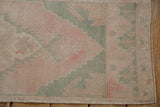 Vintage distressed Oushak rug corner, faded pink and seafoam blue stepped patterns.