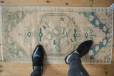 Faded cream and seafoam green distressed vintage Oushak rug mat with floral medallion.