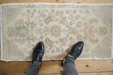 Distressed Oushak rug mat with neutral and seafoam green floral patterns shown to scale.