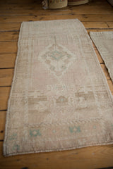 Angled perspective of a distressed Oushak rug mat showing its soft blush tones and faded teal medallion.