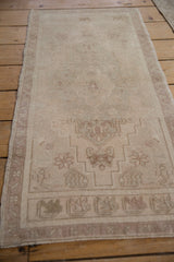 Distressed Oushak rug with faded ivory, pale mauve stepped field, and meandering border.