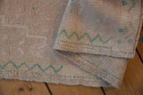 Distressed vintage Oushak rug mat with even wear, highlighting jade green zigzag motif and original side selvage.