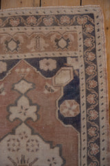 Distressed Oushak rug corner, muted coffee brown field, dusty navy floral border, and selvage.