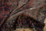 Folded section of vintage Lilihan rug: navy blue geometric border, cochineal red field, and tattered fringe.