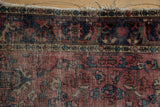 Tattered end of vintage Lilihan rug showing worn raspberry red field and border.