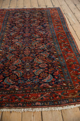 Detail of vintage Kurdish Hamadan rug's madder red floral border, navy Herati field, and white fringe.