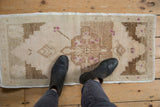 Black boots on a distressed Oushak rug, featuring geometric brown patterns and purple blossoms.