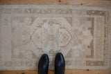 Distressed Oushak rug with faded beige floral patterns and subtle green accents.