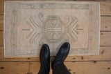 Distressed vintage Oushak rug with muted cream, sage green floral medallion, styled with boots.