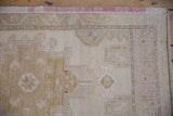 Distressed Oushak rug pile with faded geometric pattern in ivory and sand.