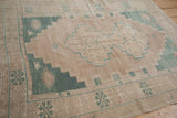 Distressed vintage Oushak rug corner showing camel field, green stepped spandrel, floral gul border.
