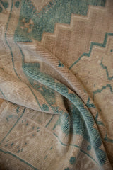 Folded vintage Oushak rug pile revealing camel, beige, and faded emerald green stepped pattern.