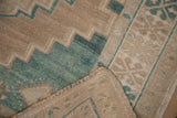 Distressed Oushak rug's folded corner reveals even wear across knot heads and celadon green.