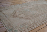 Distressed Oushak rug texture revealing faded geometric motifs in cream, brown, and dusty blue.