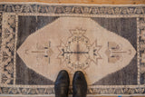 Vintage distressed Oushak rug with an oxidized silver and beige floral medallion, shown with boots.