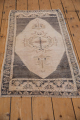 Distressed Oushak rug corner, revealing soft ivory pile, stepped overlay, and meandering vine border.