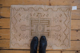 Distressed beige Oushak rug, with dusty bronze geometric patterns and black boots.
