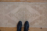 Vintage distressed Oushak runner's subtle faded pattern and soft beige tones with black boots.