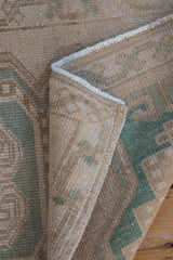 Vintage Distressed Oushak rug texture showing cream, sand, and dusty jade green with intact selvage.