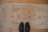 Distressed vintage Oushak runner with faded cream, sand, and pale green floral patterns.